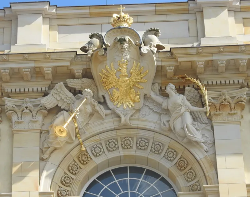 Golden double-headed eagle with angels, crown, and rosettes on building facade